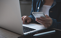A person holding a smart phone working on a computer