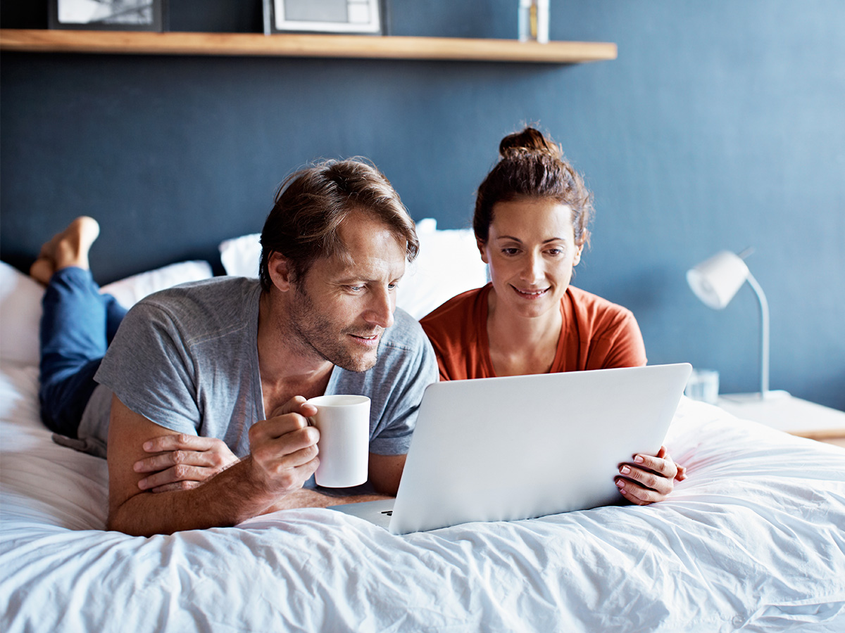 A couple on a bed working on a laptop
