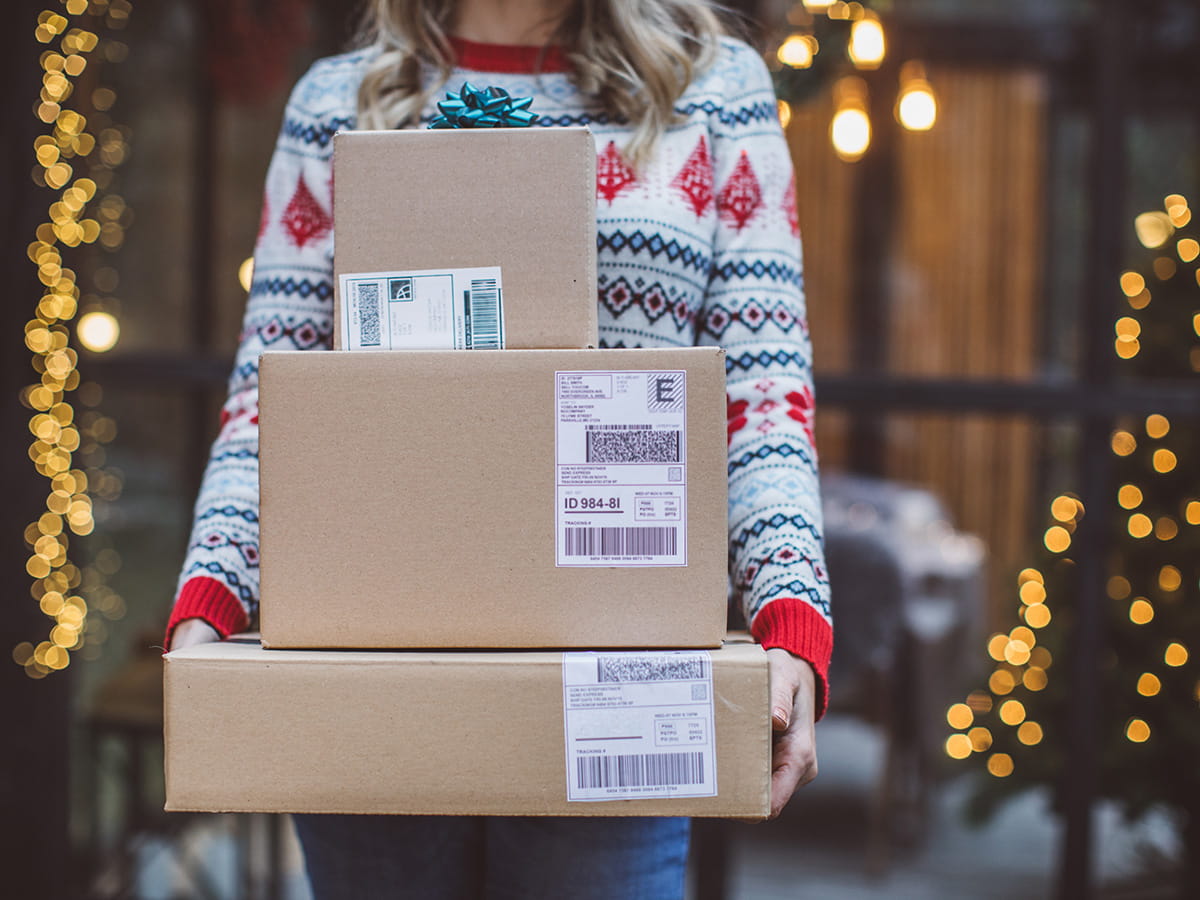 A woman wearing a festive sweater carrying gift boxes