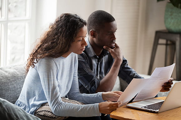 a couple with paperwork working together at a laptop 